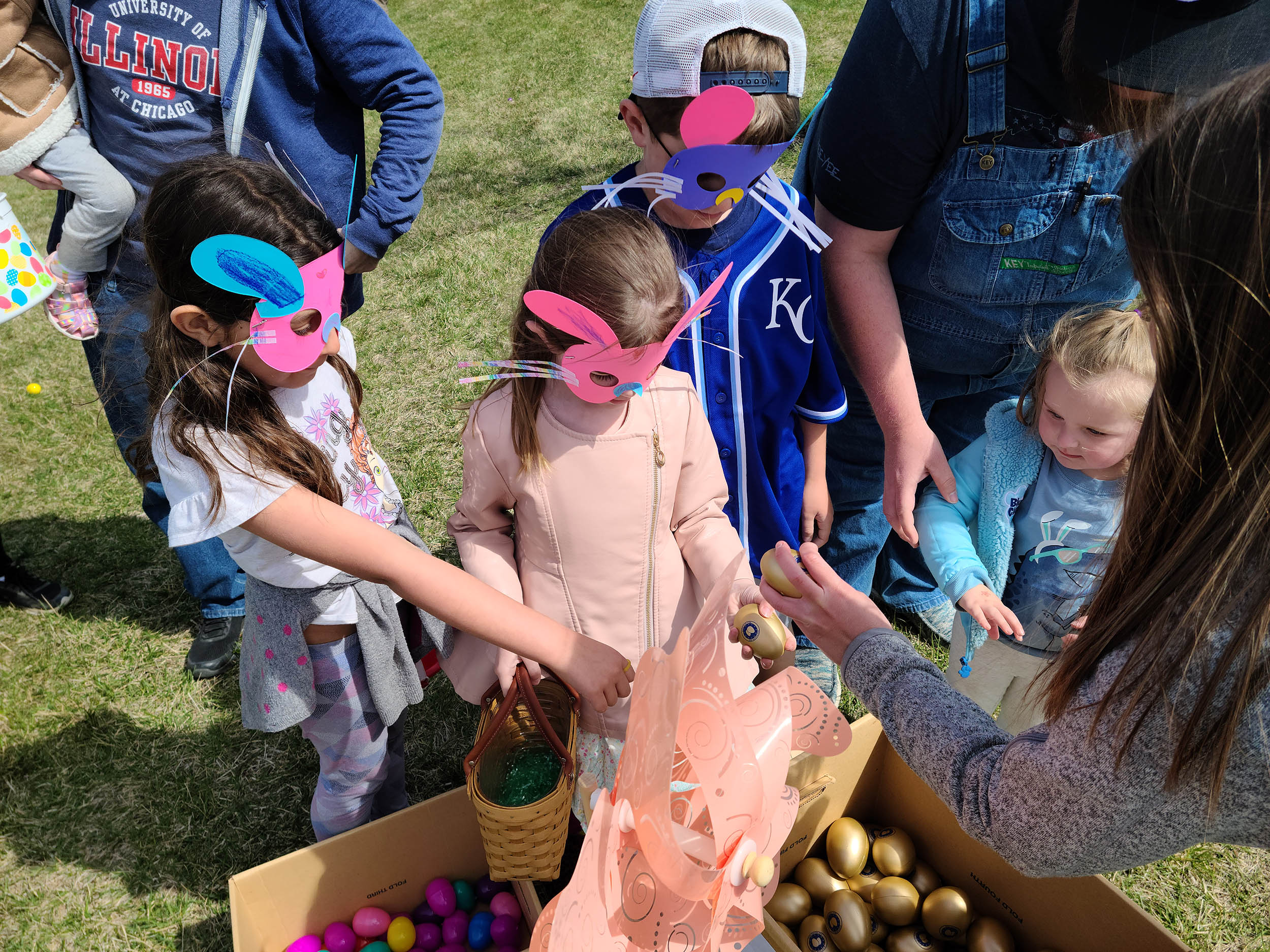 children in bunny masks stand around a box of golden Easter eggs