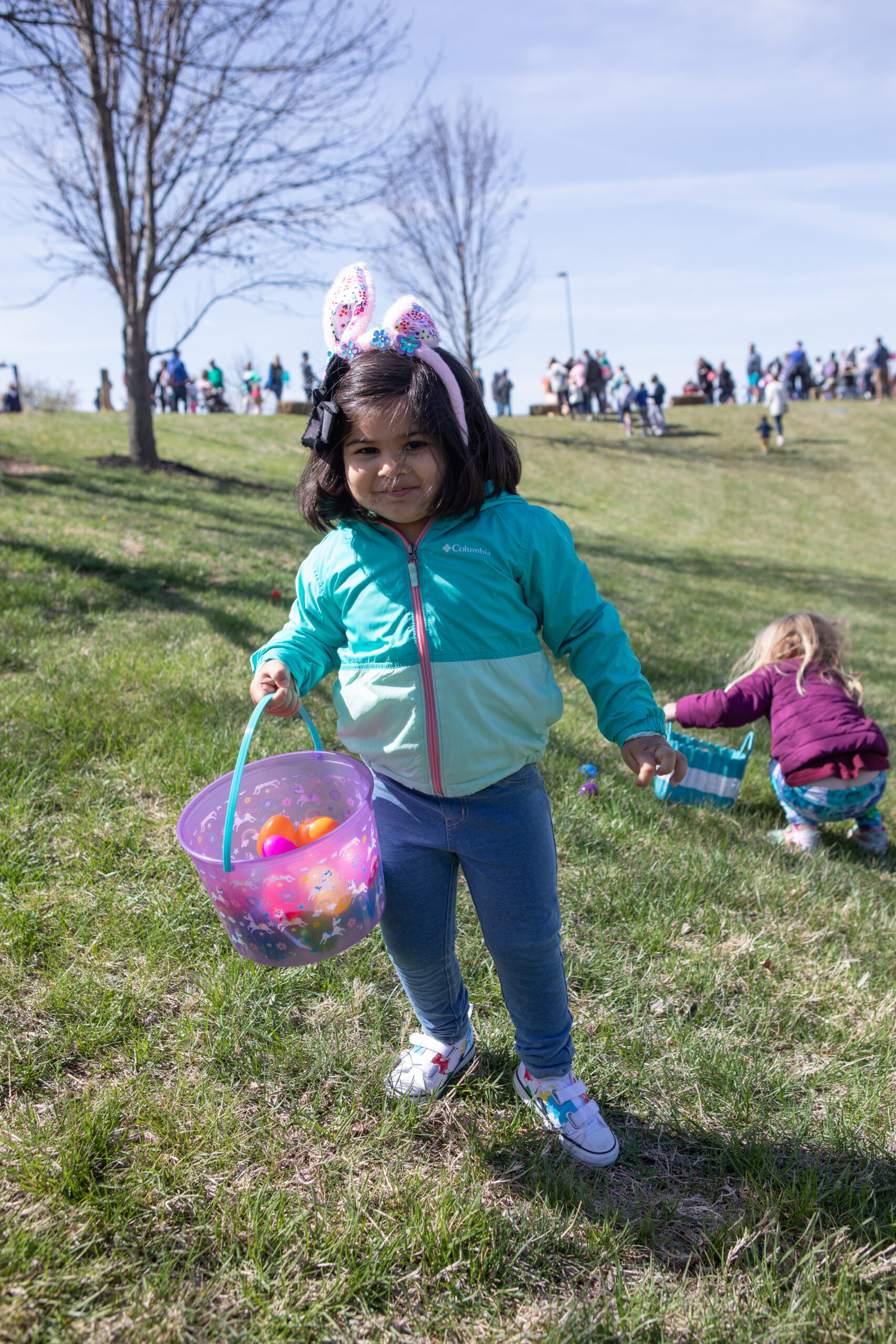 A girl with a bunny ears headband stands smiling on the lawn outside the Dole Institute, holding a basket of plastic eggs