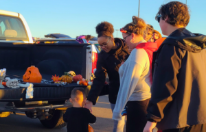 A woman hands a child candy during a Trunk or Treat event while their parents look on.