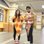 Students wearing pizza costumes pose for a photo while holding flyers for an event.