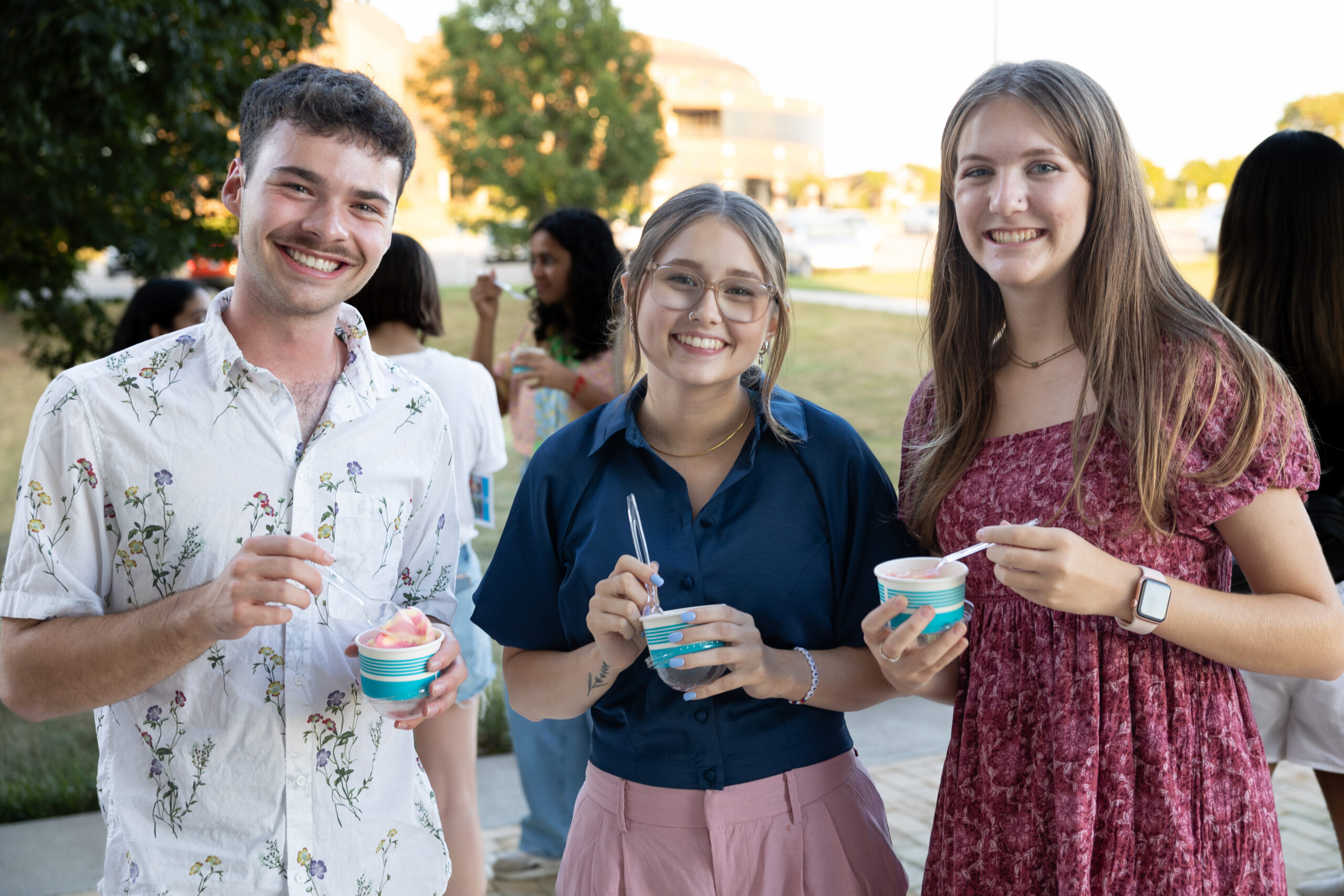 A group of people stand and smile together outside while holding small cups of ice cream.