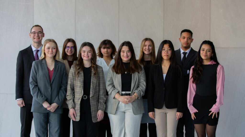 A group of ten students gather in front of a grey wall for a photograph. 