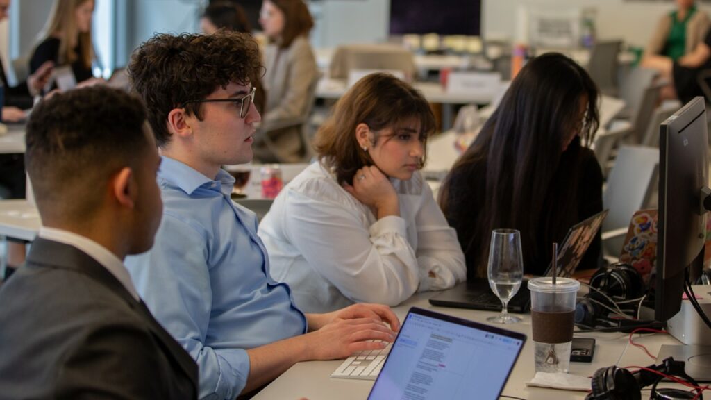 Four people gather around a computer to work on project.